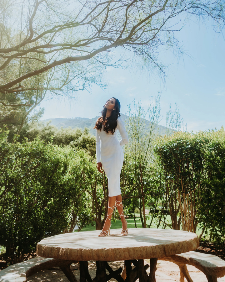 Diya Patel standing on a table in a white dress looking up at the sunlight